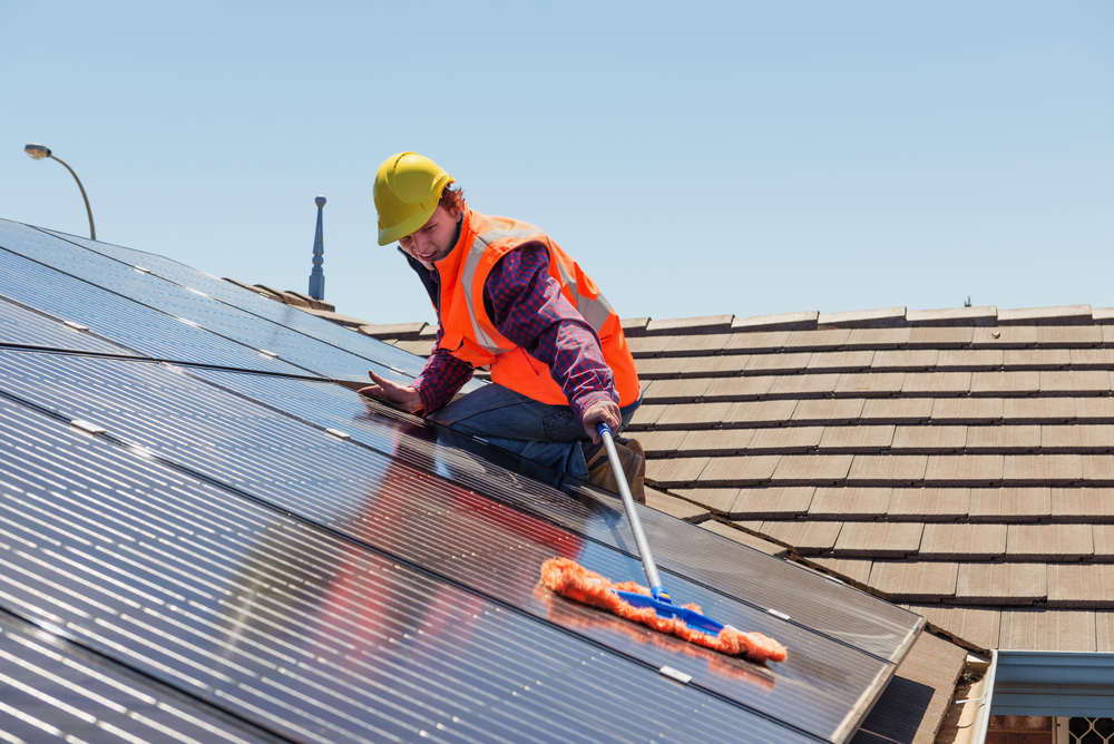 Young worker cleaning solar panels on the roof